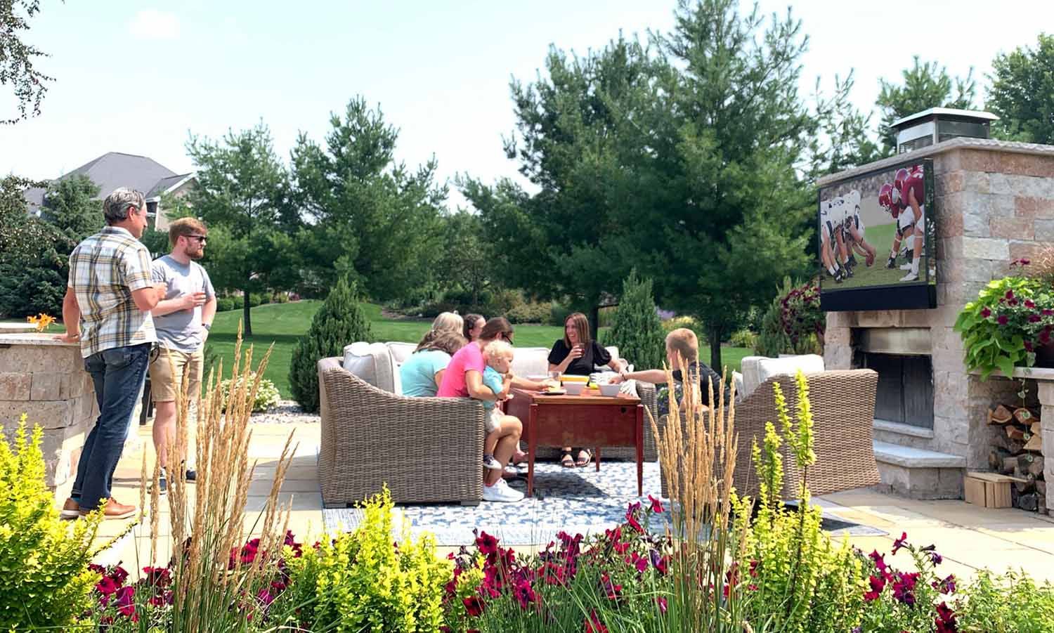 a group of friends sitting outside in front of an outdoor tv