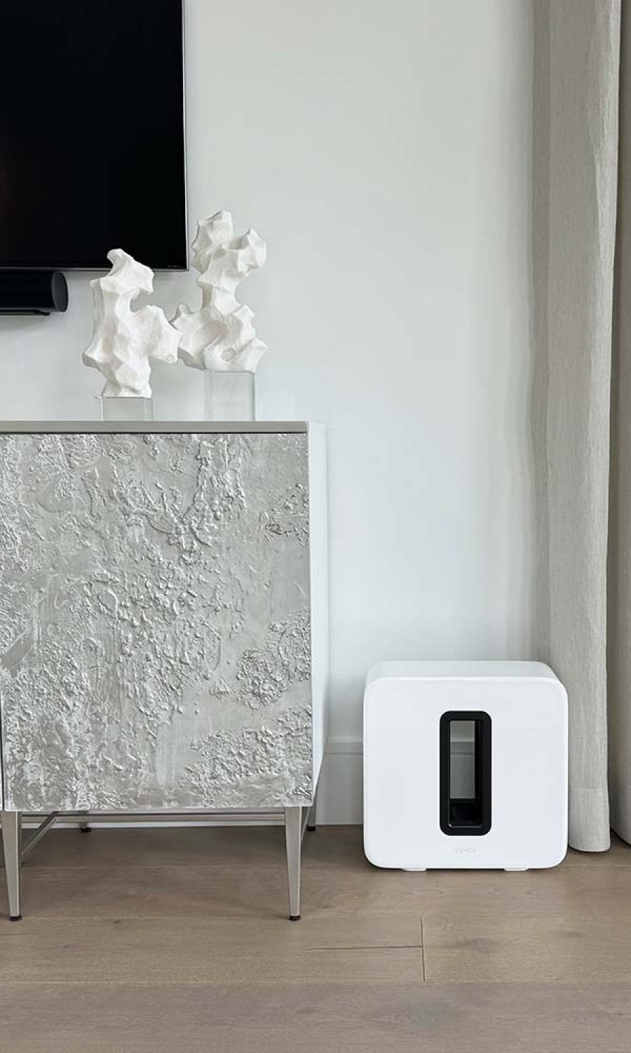 Sonos sub speaker on a wooden floor next to a piece of furniture