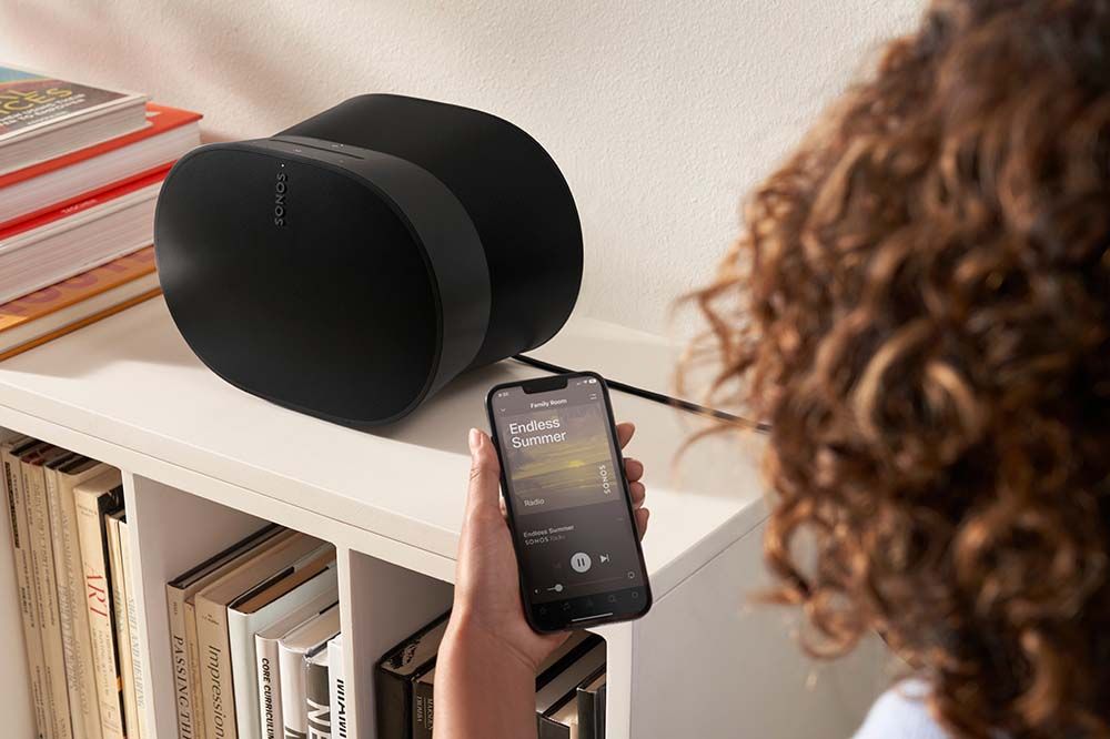 woman looking at a phone in front of a sonos speaker